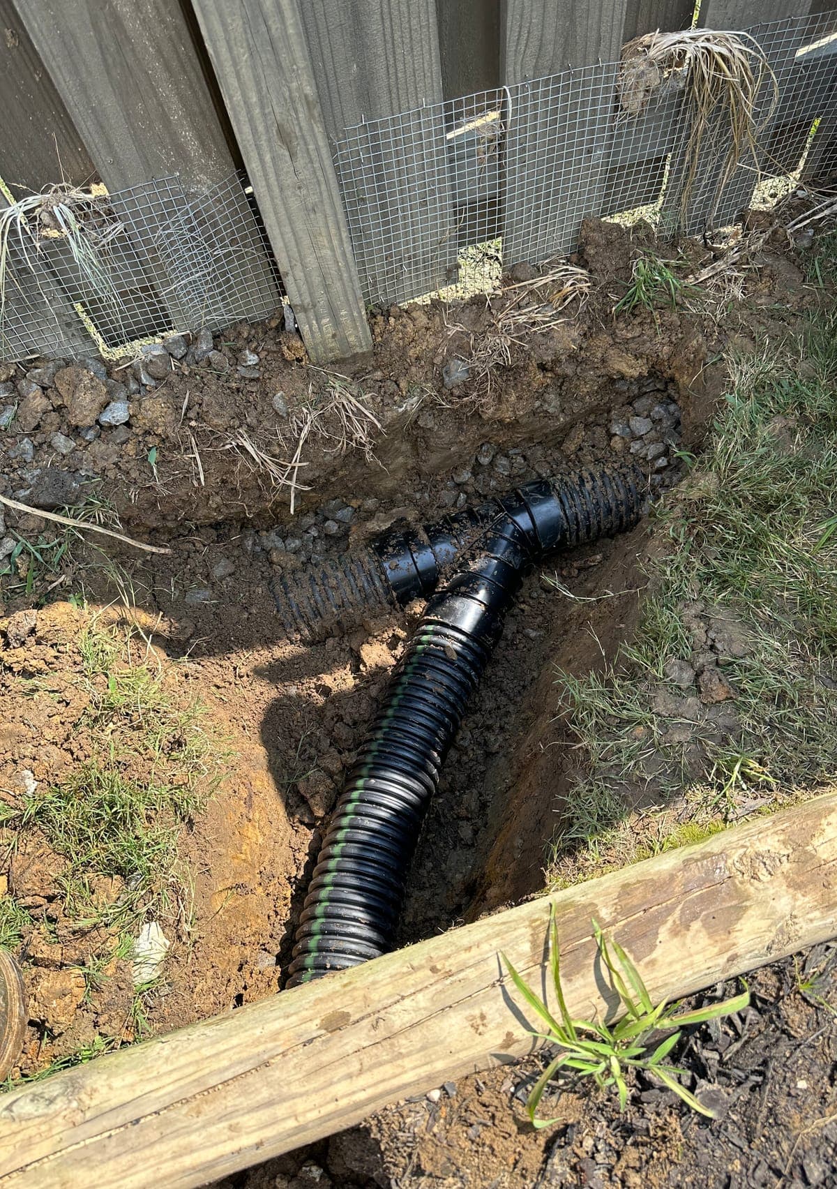 Two drain lines joined with a wye fitting in a gravel bedded trench, ready to be backfilled.