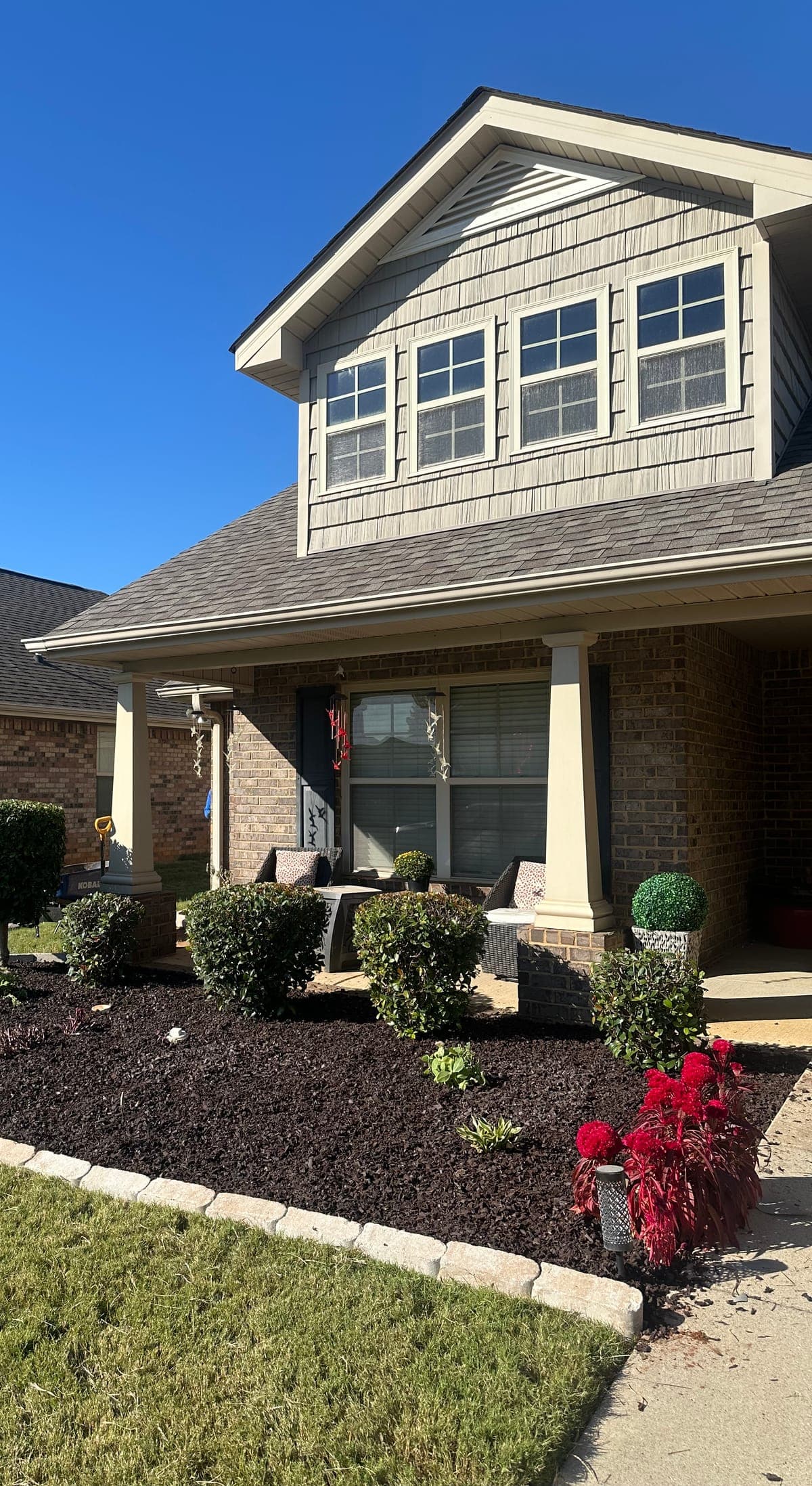 A curved front bed laid out along a two story brick home, stone edged and planted with clipped shrubs and a small topiary.