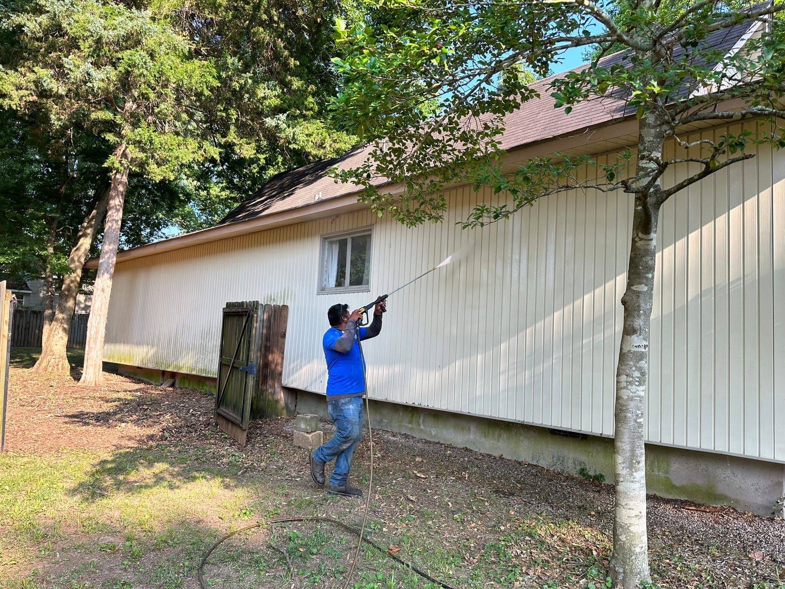A crew member washing years of green off a long stretch of house siding, the clean panels showing pale against the rest.
