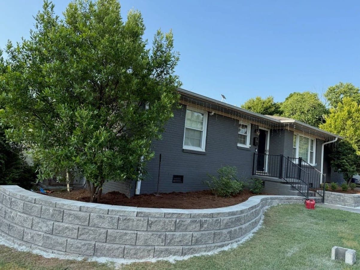 A curved block retaining wall wrapping a fresh planting bed around the front of a gray brick home.