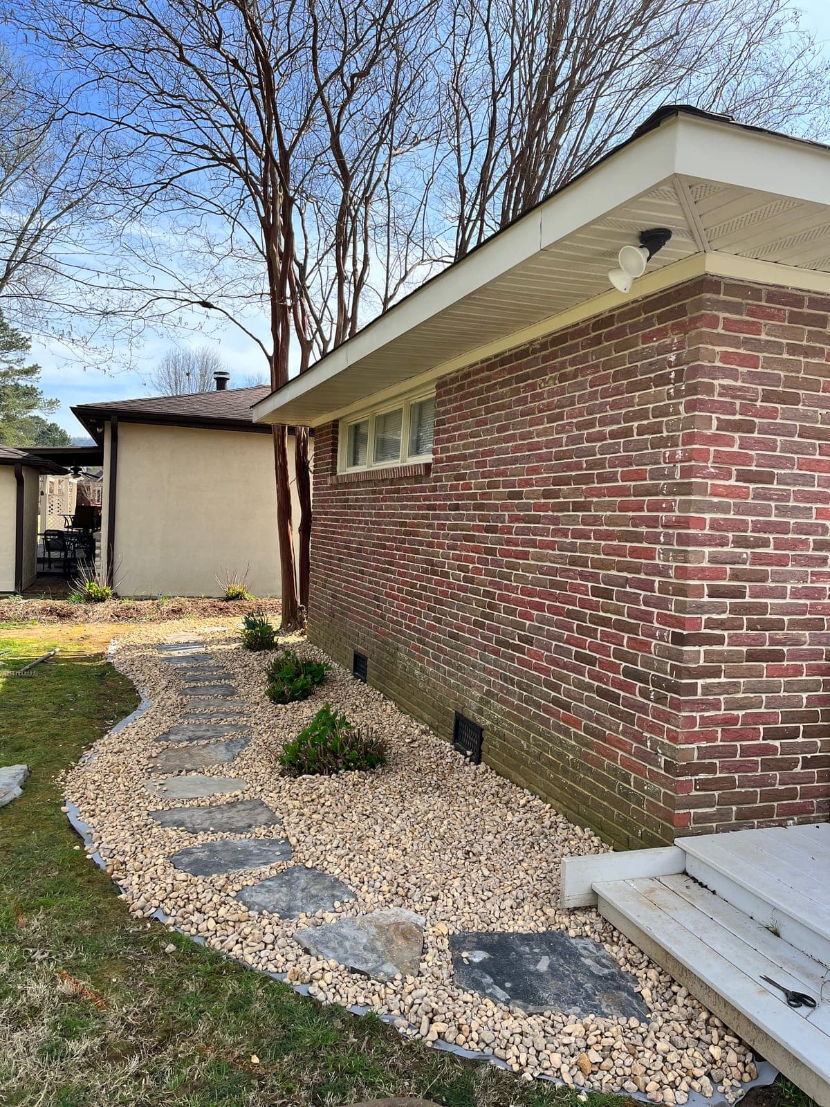 Flagstone steppers set into a river rock bed running the length of a brick house to the back steps.