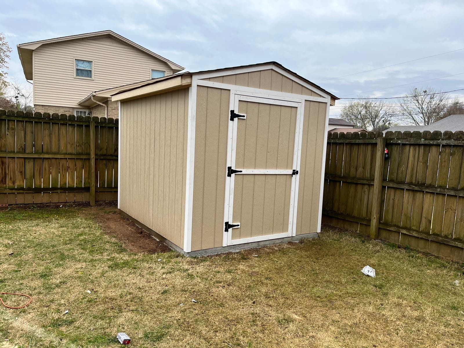 A finished storage shed with a white trimmed door, set square on its concrete pad against a wood fence.