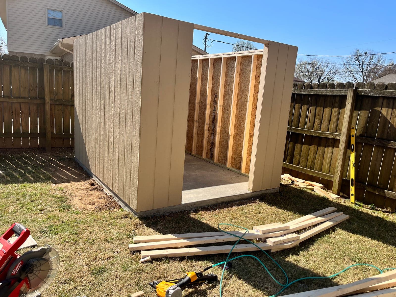 A shed part way through its build, walls sheathed and square on the pad with the door opening framed out.