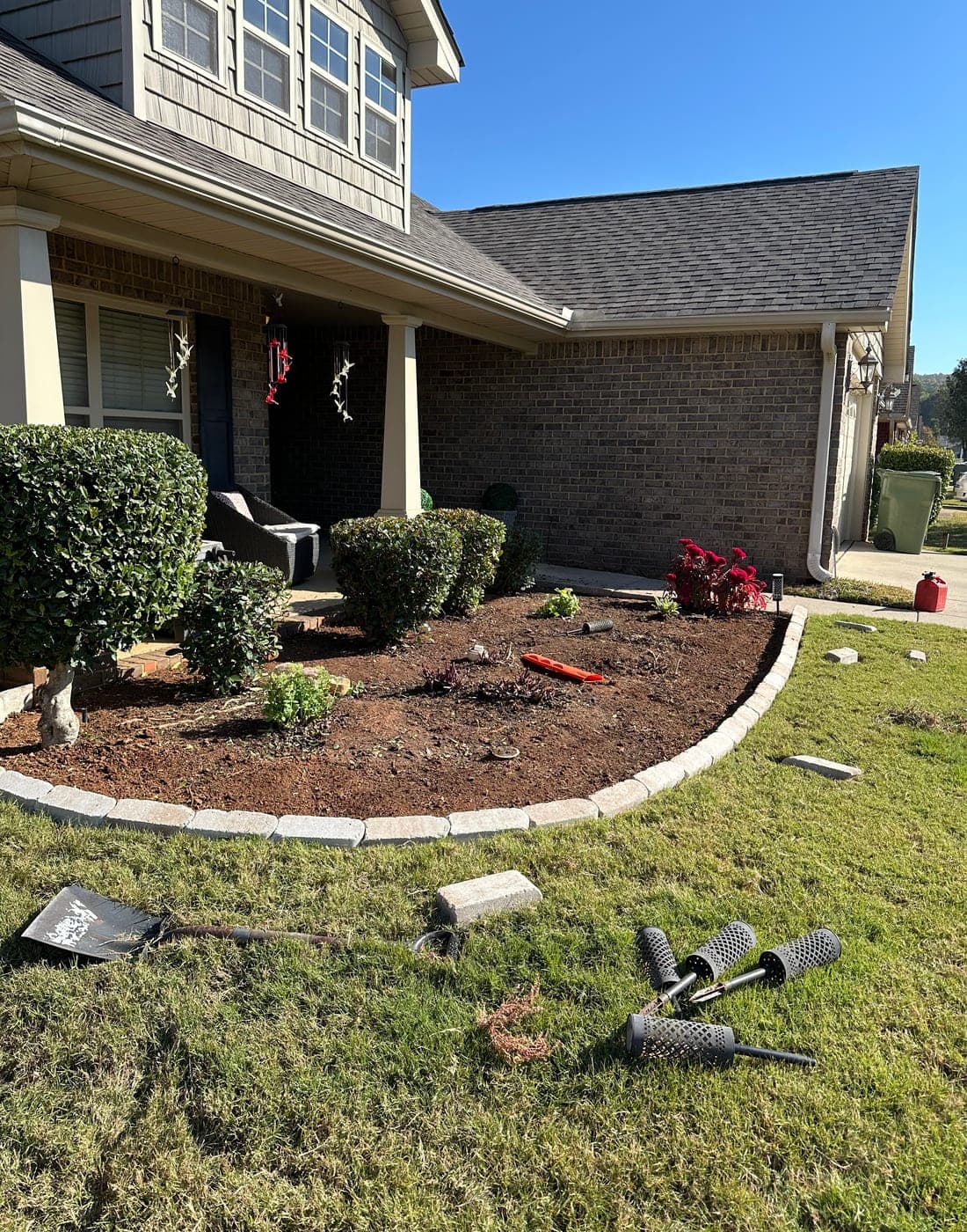 A front planting bed stripped to bare dirt with a tan paver edge freshly set along its curve.