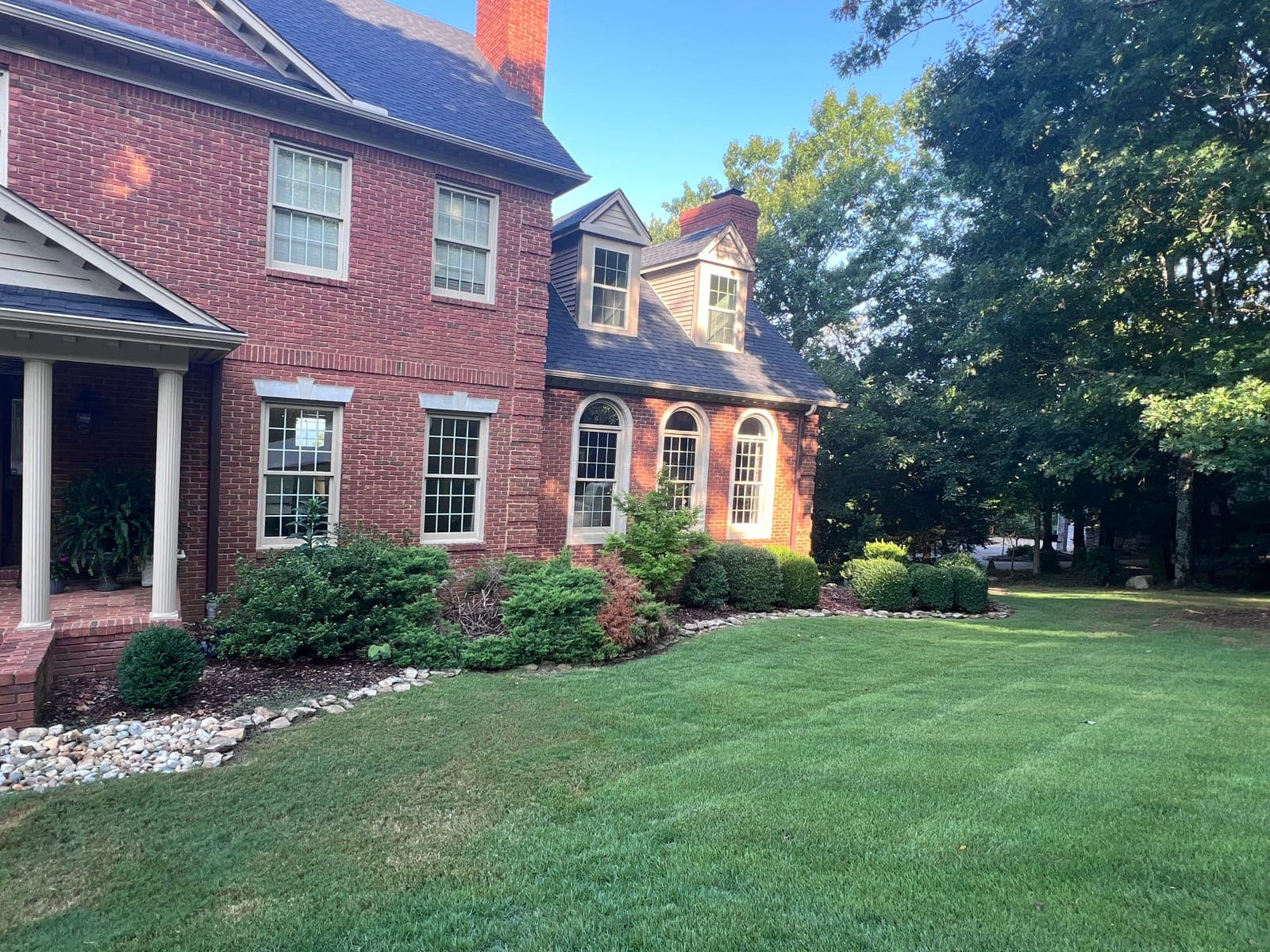 The front beds of a brick home crowded with older mixed shrubs, dead branches showing at the center of the bed.